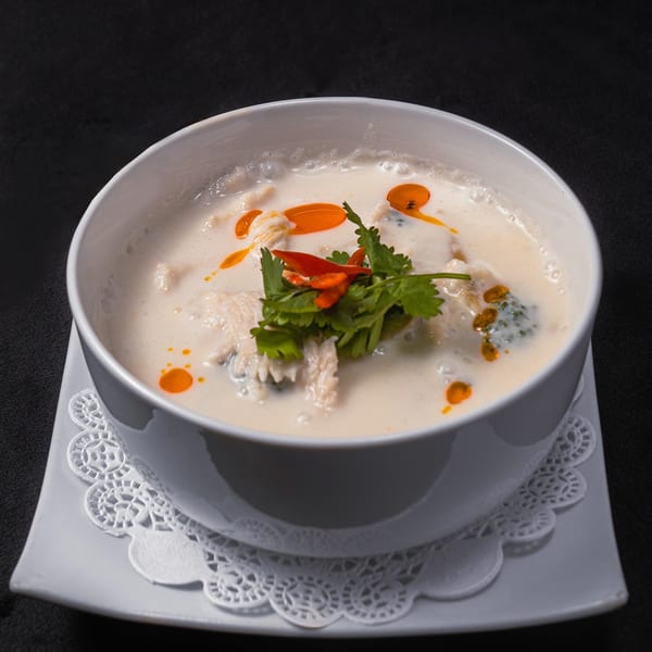 Creamy coconut soup with chicken, cilantro, and chili oil in a white bowl on a dark background.