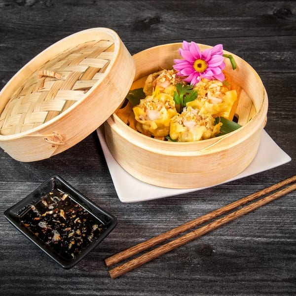 Steamed dumplings with a pink flower in a bamboo steamer, with chopsticks and sauce.