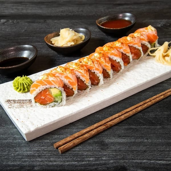 Salmon and avocado sushi roll with wasabi, ginger, and soy sauce on a white plate.