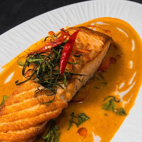 Pan-seared salmon fillet with red curry sauce, topped with chilies and kaffir lime leaves.