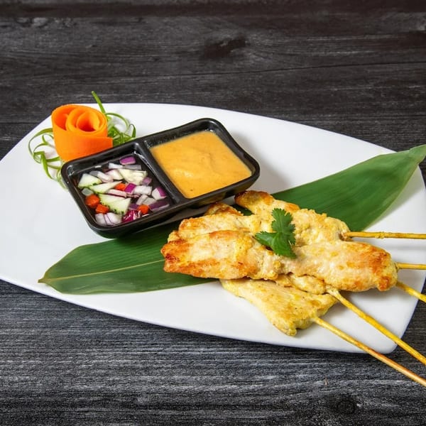 Chicken satay skewers with peanut sauce and cucumber relish, garnished with a carrot rose.