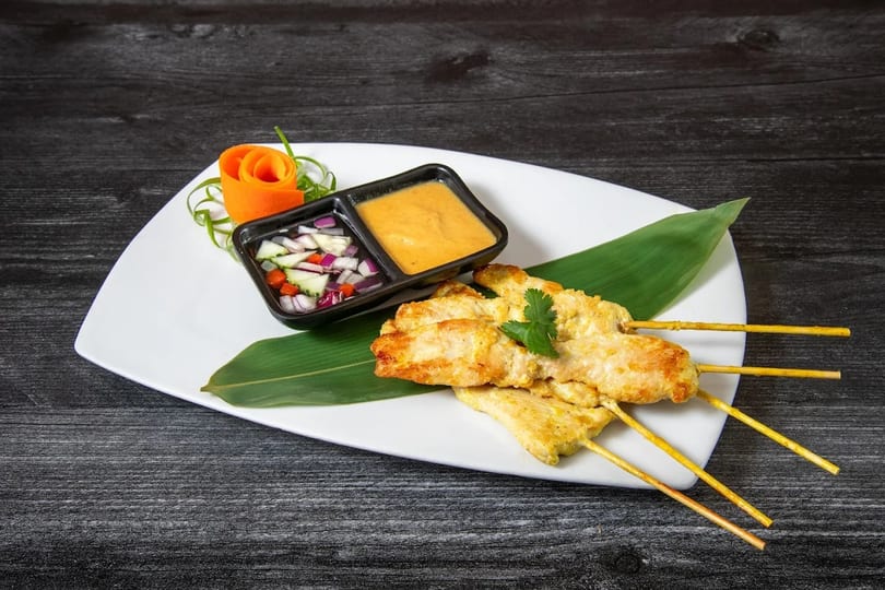 Chicken satay skewers with peanut sauce and cucumber relish, garnished with a carrot rose.