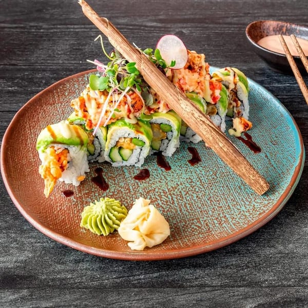 Sushi rolls with avocado, tempura, and spicy topping, garnished with microgreens, wasabi, and ginger.