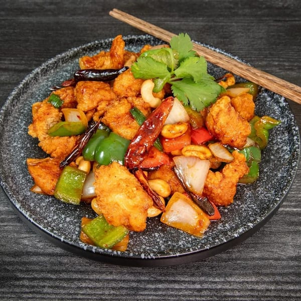 Kung Pao chicken with cashews, peppers, onions, and dried chilies on a dark plate with chopsticks.