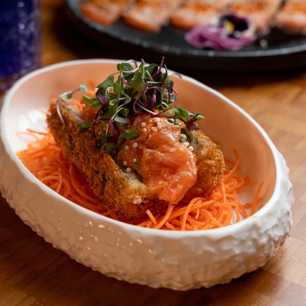 Crispy fried sushi roll topped with salmon, microgreens, and tobiko, served on shredded carrots.