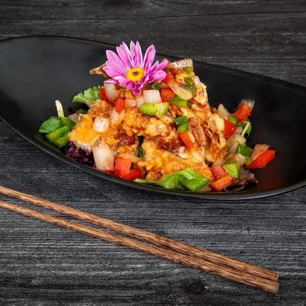Crispy fried soft-shell crab with bell peppers, onions, and a pink flower garnish on a black plate.