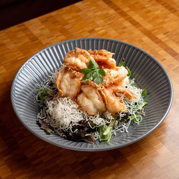 Crispy fried shrimp with vermicelli noodles and mixed greens on a gray plate.