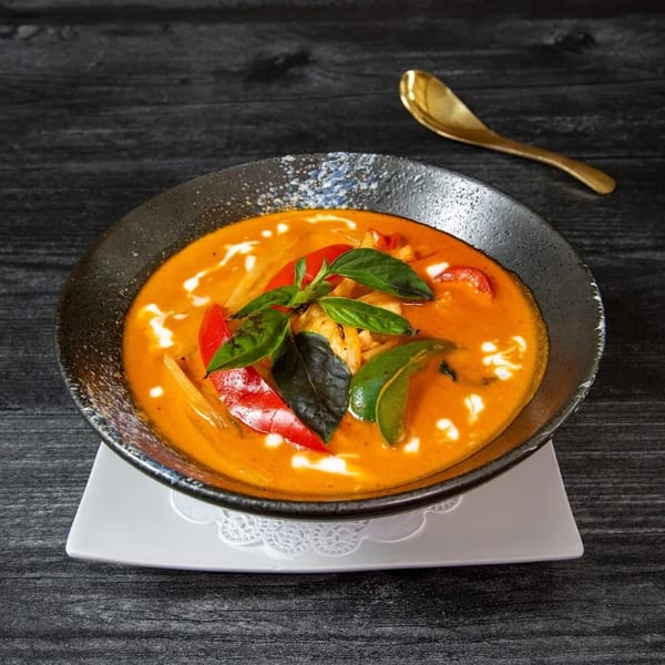Red curry with chicken, red peppers, and basil in a dark bowl on a black wooden table.