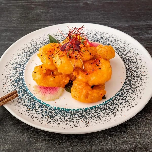 Crispy orange shrimp with red chili threads, black sesame seeds, and radish on a white plate.