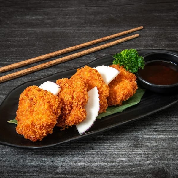 Crispy fried shrimp cakes with radish slices, parsley, and dipping sauce on a black plate with chopsticks.