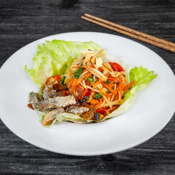 Som Tum salad with crispy fish skin and lettuce wraps on a white plate with chopsticks.