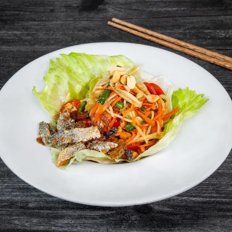 Som Tum salad with crispy fish skin and lettuce wraps on a white plate with chopsticks.