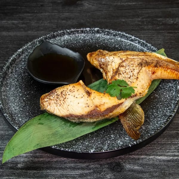 Grilled fish with a crispy skin, garnished with cilantro and served with a dark sauce.