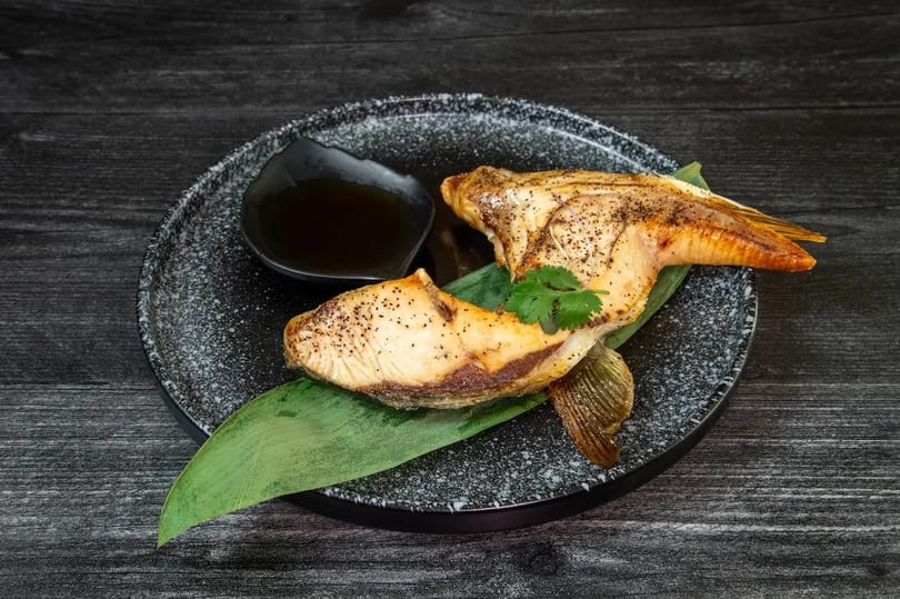 Grilled fish with a crispy skin, garnished with cilantro and served with a dark sauce.