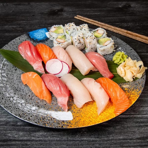 Assorted sushi and sashimi platter with California rolls, ginger, and wasabi on a dark table.