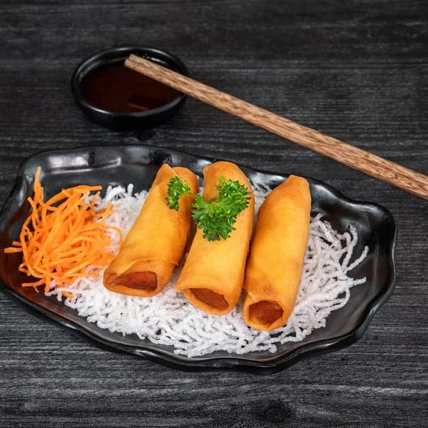 Three golden spring rolls with parsley, shredded carrots, and white noodles on a black plate.