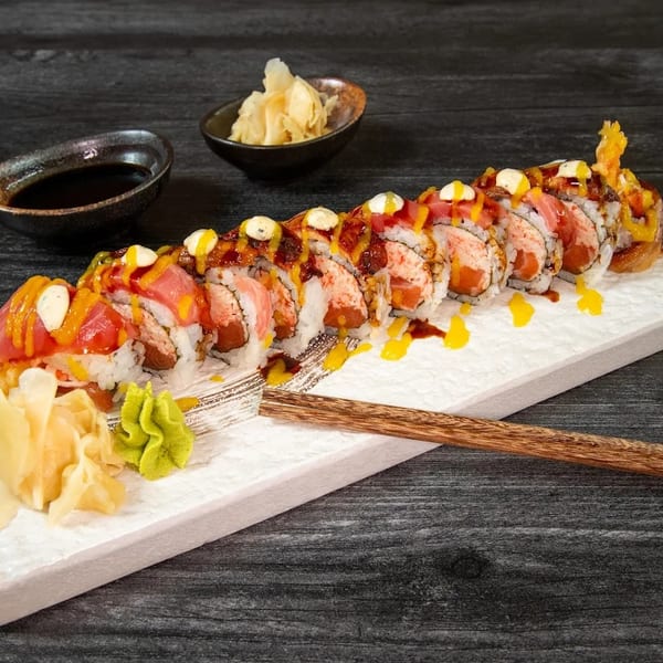 A long sushi roll with tuna, salmon, and sauces, served with ginger and wasabi.
