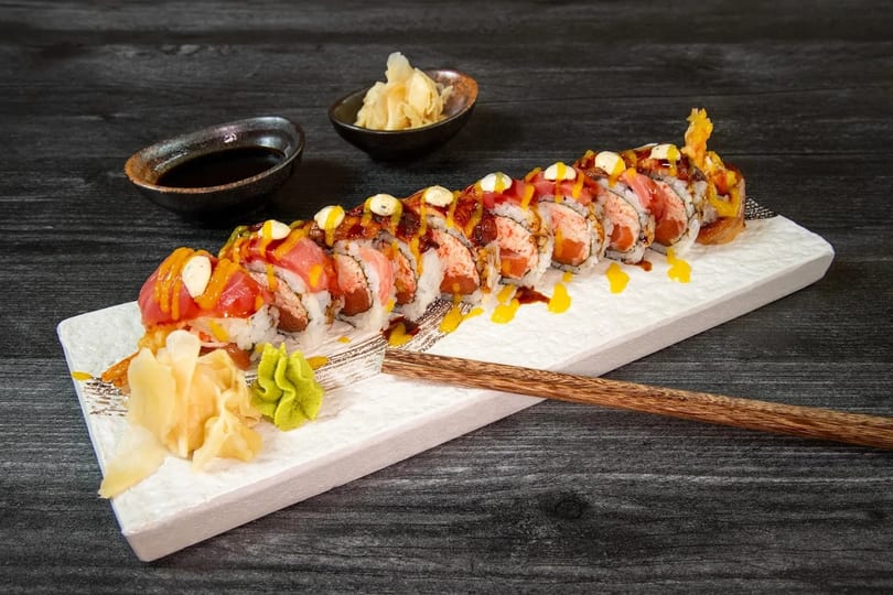 A long sushi roll with tuna, salmon, and sauces, served with ginger and wasabi.