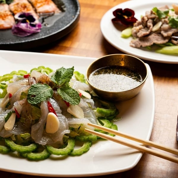 A vibrant spread of Thai dishes, including a shrimp salad, grilled salmon, beef, and a blue cocktail.