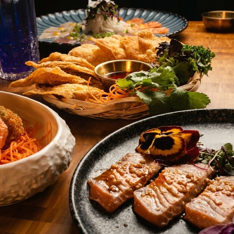A table laden with various Asian dishes, including salmon, fried wontons, and a blue drink.