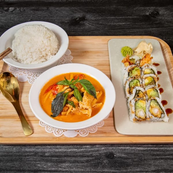 Red curry with chicken and basil, white rice, and shrimp tempura sushi rolls on a wooden tray.